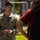 A U.S. Army soldier named Pitsikos, wearing OCP (Operational Camouflage Pattern) uniform, is engaged in conversation with a civilian wearing a red shirt and a backpack from Foothill Regional Medical Center. The interaction appears to be taking place outdoors on a sunny day, likely at a community or medical outreach event. The soldier appears to be speaking or listening attentively.