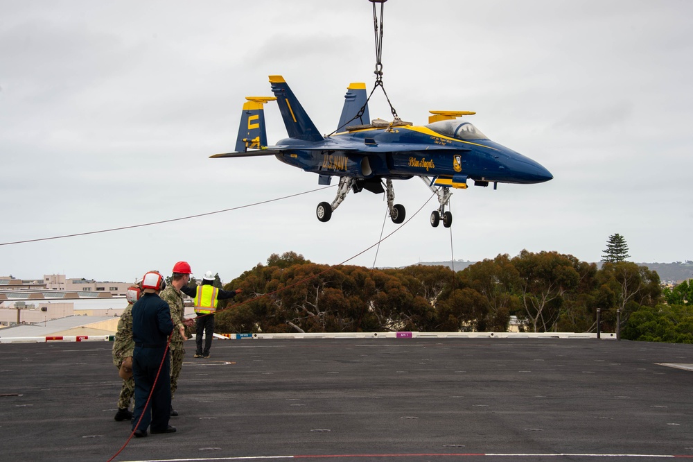 Sailors and civilian personnel transport an F/A-18 super hornet Blue Angel onto the flight deck of Nimitz-class aircraft carrier USS Carl Vinson