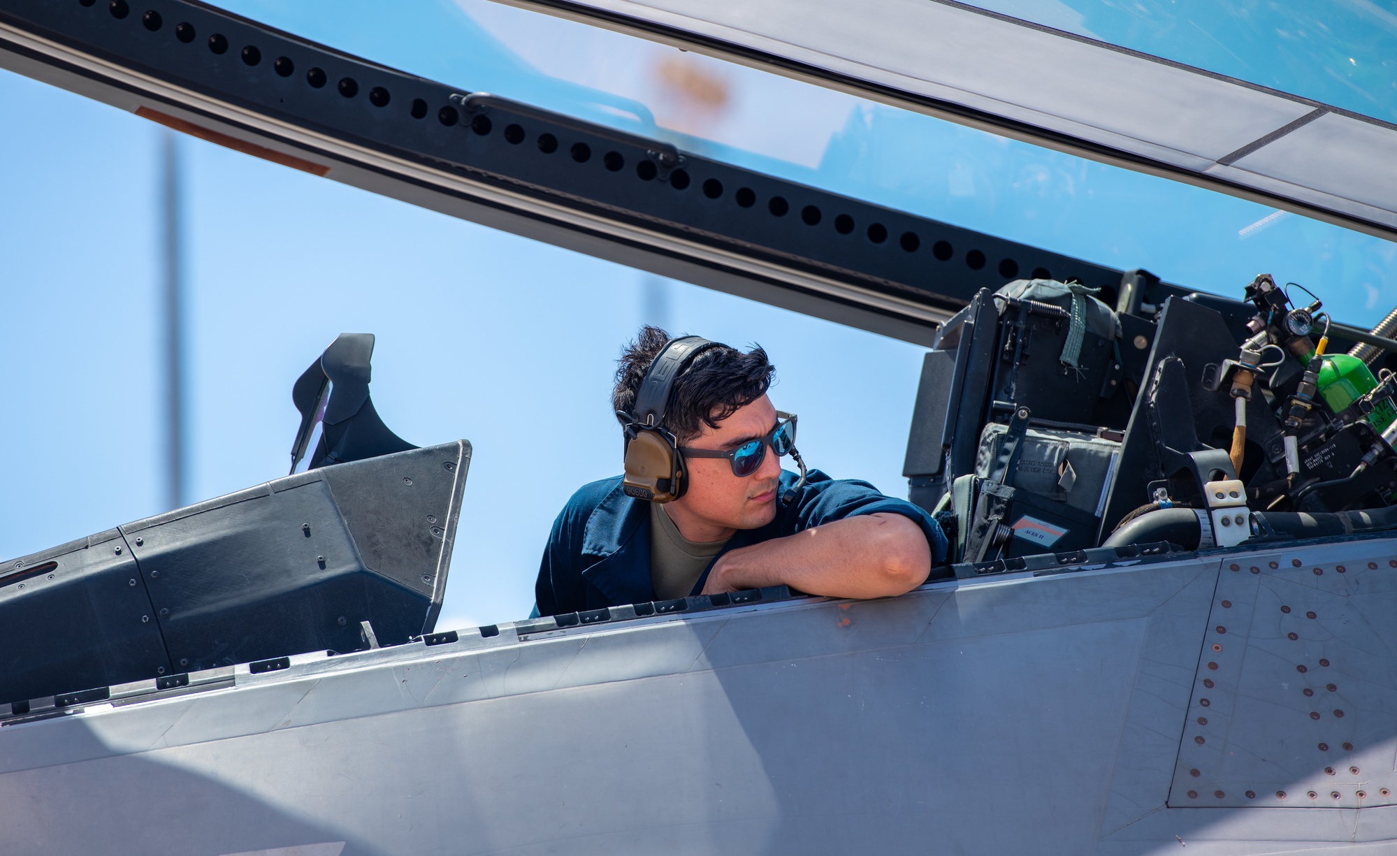 A maintainer working in an F-22 cockpit beneath its open canopy.