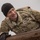Ivy Week 2022 Mabry Mile: Keep pushing through A U.S. Army soldier wearing OCP (Operational Camouflage Pattern) uniform is climbing over a wooden obstacle, likely on a military obstacle course. The soldier, identified by name tape as 'MAVRINA,' is wearing a black beanie cap and tactical gloves. The image captures a moment of physical exertion with the soldier appearing to strain while pulling themselves over the wooden barrier.