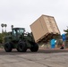 A tram moves conex boxes off of a Landing Craft Utility