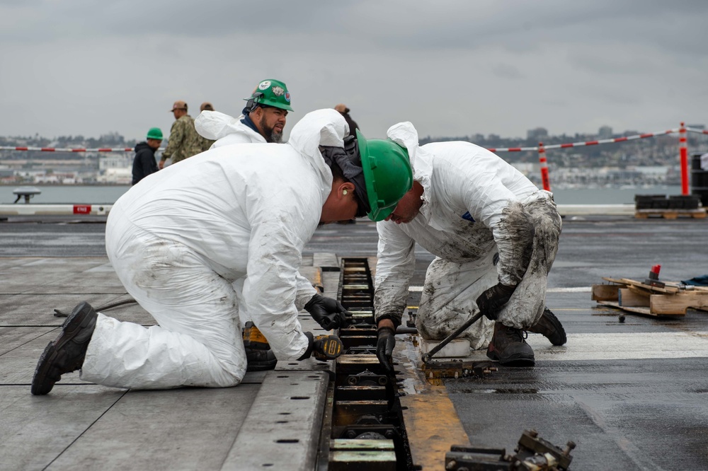 Civilian personnel conduct maintenance on a jet blast deflect the flight deck of USS Carl Vinson (CVN70)