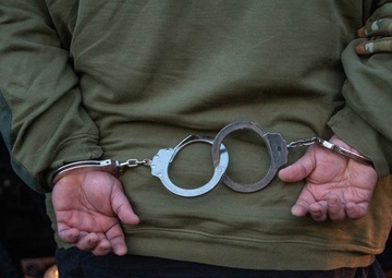 An arrested individual is walked to a law enforcement vehicle by ICE Enforcement and Removal Operations (ERO) deportation officers