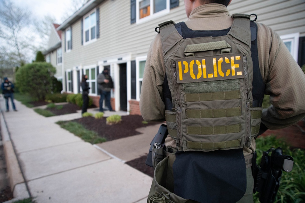 ICE Enforcement and Removal Operations (ERO) deportation officers provide perimeter security while other officers advise a spouse of her husband's arrest