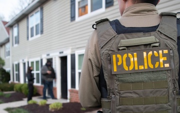 ICE Enforcement and Removal Operations (ERO) deportation officers provide perimeter security while other officers advise a spouse of her husband's arrest