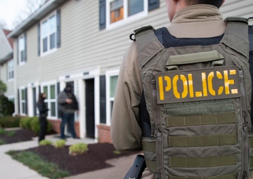 ICE Enforcement and Removal Operations (ERO) deportation officers provide perimeter security while other officers advise a spouse of her husband's arrest