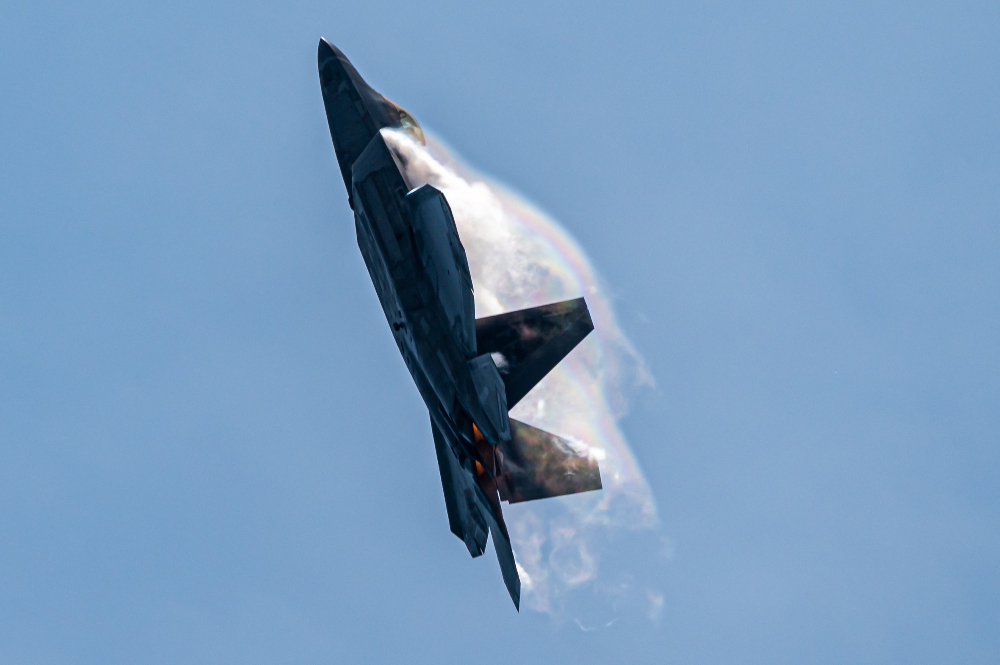An F-22 in a steep nose-up attitude during a flight demonstration, with its wings, twin tails, and two engine exhausts visible.