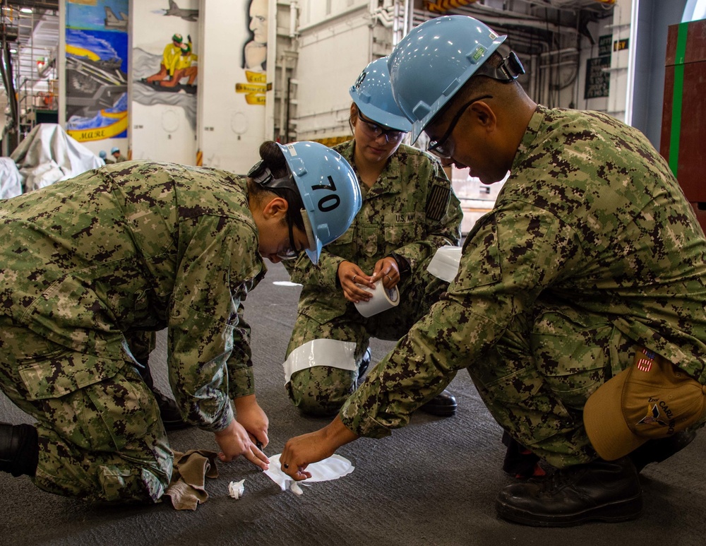 Sailors perform maintenance in the hangar bay of USS Carl Vinson (CVN 70)