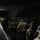 Headquarters Battalion Conditioning Hike A large group of military personnel in camouflage uniforms and full gear are marching in formation toward and through an underpass or tunnel at night. Many individuals are wearing high-visibility yellow reflective bands on their arms or torsos, likely for safety during the nighttime movement. The scene appears to be a military ruck march or training exercise conducted in low-light conditions.