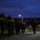 Headquarters Battalion Conditioning Hike A column of military personnel in full combat gear and rucksacks marches along a paved road during twilight or pre-dawn hours. The soldiers are equipped with large backpacks and wear high-visibility yellow and red reflective bands for safety during the low-light ruck march. A single street lamp illuminates the path ahead, with buildings and trees visible in the background.