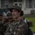 Headquarters Battalion Conditioning Hike The image shows a U.S. Marine in MARPAT woodland digital camouflage uniform, appearing to be engaged in a training or operational activity. The Marine is wearing a cover (cap) and has a gold oak leaf insignia visible on the collar, indicating the rank of Major. Other personnel in similar uniforms are visible in the background.
