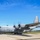A U.S. Air Force C-130 Hercules military transport aircraft assigned to the Ohio Air National Guard is taxiing on a runway apron. The aircraft is painted in standard gray military livery and has all four turboprop engines running, as evidenced by the spinning propeller blur. The setting appears to be a military or joint-use airfield on a clear, sunny day.