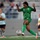 A women's football match is in progress, with a player in a green kit (number 3) about to strike the ball. The green-kitted player appears to represent Cameroon, based on the visible badge featuring the Cameroonian flag colors on her jersey. Opposing players in light blue and black kits, consistent with Belgium's colors, are visible in the background.