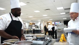 Culinary Specialist 2nd Class Bradley Simpkins, right, assigned to Naval Air Station (NAS) Joint Reserve Base (JRB) Fort Worth speaks to the judge during the Commander, Navy Installations Command (CNIC) Food Services Ashore Culinary Competition