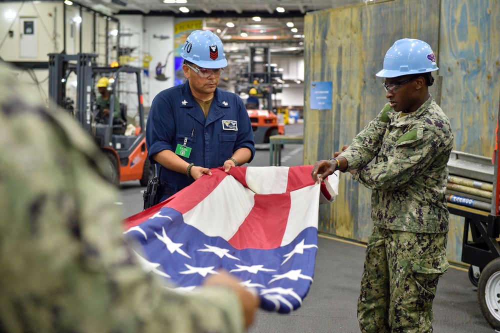 Sailors fold the ensign in the hangar bay of Nimitz-class aircraft carrier USS Carl Vinson