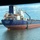 The image shows a large commercial tanker vessel named 'Hafnia Rhine', registered in Singapore with IMO number 9341940. The ship is navigating on a calm waterway, viewed from underneath a bridge or overpass structure. The vessel displays the Hafnia company livery with a blue hull, white superstructure, and the distinctive green circular logo on the funnel.