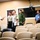 A group of five military and law enforcement personnel in various uniforms are gathered in what appears to be a briefing room or auditorium with rows of empty tan chairs. One individual in a white shirt with a yellow stripe is gesturing and speaking to the others, suggesting a briefing or orientation is taking place. The uniforms represent multiple nationalities or agencies, indicating a multinational or inter-agency meeting.
