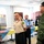 A group of military personnel in various uniforms are engaged in conversation in what appears to be an indoor meeting or reception area. The individuals represent multiple nations based on their distinct uniforms and insignia. The setting includes tables with colorful coverings, suggesting a cultural or diplomatic gathering event.