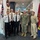 A group of seven military personnel pose for a formal photograph in what appears to be an Australian naval headquarters corridor. The group includes personnel in Australian Navy white dress uniforms, US Navy NWU Type III camouflage, a US Navy khaki service uniform, and a flight suit. A circular 'Chief of Navy' emblem and the Australian national flag are visible in the background.