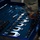 A person wearing military camouflage uniform is reaching into an open tool drawer or case lined with blue foam padding. The drawer contains an organized set of chrome/silver hand tools including crowfoot wrenches, socket sets, screwdrivers, and extensions arranged in custom-cut foam slots. Several tool slots appear empty, suggesting tools have been removed or are being inventoried.