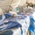 The image shows a field surgical setup inside what appears to be a military or emergency medical tent. A long table covered with blue sterile draping holds numerous surgical instruments laid out in preparation for procedures. The setting suggests a forward operating base or disaster relief surgical unit.