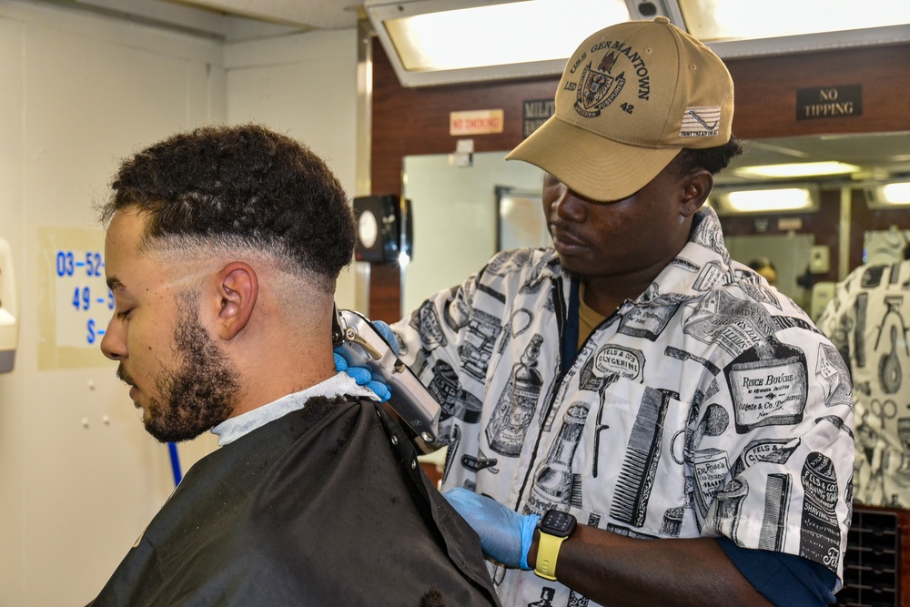 Seaman Martin Blake cuts Petty Officer Third Class Kevin Strader's hair during the full management review on aboard the USS Germantown on Aug 31. 2022.