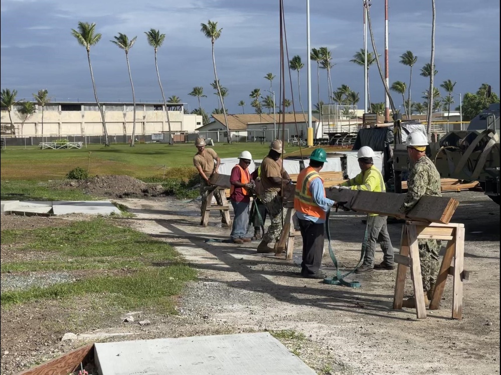 Seabees work with Marshallese contractors to lift and place a ridge beam for the Richardson Multipurpose Facility project.