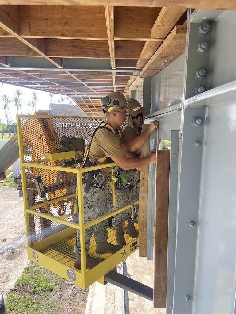 Equipment Operator 3rd Class Francisco Ramirez and Steelworker 3rd Class Daniel Ceren, install steel fascia on the Richardson the Multipurpose Facility.
