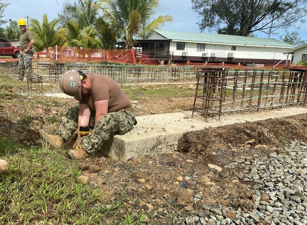 Construction Electrician 2nd Class Siyu Tibbs uses a hammer drill to drill through the end of the footers to add rebar dowels.