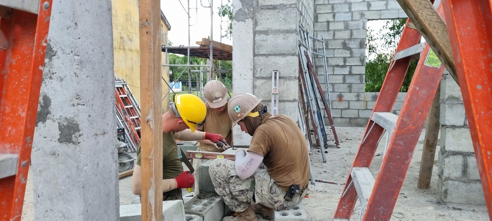 Seabees and Marines level a course of Concrete Masonry Units block for the Phước Hòa primary school in Vietnam.