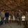 A group of people, including several U.S. Army soldiers in MultiCam/OCP camouflage uniforms and civilians, are gathered inside a geodesic dome structure. The soldiers appear to be briefing or presenting to the civilian group, with one soldier holding papers. The setting appears to be a military or educational facility.