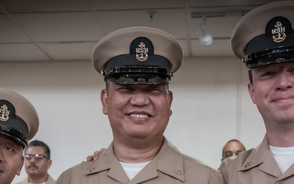 Three U.S. Navy Chief Petty Officers in Service Khaki (Class B) uniforms pose together for a group photo, smiling at the camera. All three wear the distinctive CPO combination cover (garrison cap) with the USN anchor insignia. The central and right figures display multiple service ribbons and warfare qualification badges on their uniforms.