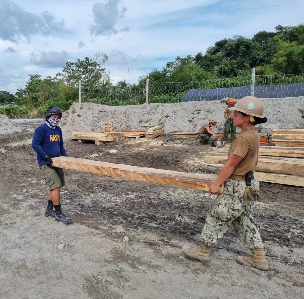 Builder 3rd Class Hannah Dodge with Naval Construction Battalion (NMCB) 4, hauls a 6x8 posts to the build site of a sentry post.
