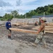 Builder 3rd Class Hannah Dodge with Naval Construction Battalion (NMCB) 4, hauls a 6x8 posts to the build site of a sentry post.