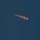 SLD 45 supports the first National Security Space Launch mission on a Falcon Heavy rocket A rocket or missile is captured in flight against a deep blue sky, trailing a large orange-red plume of exhaust or fire behind it. The object appears to be traveling at high speed on a roughly horizontal trajectory. The bright orange exhaust cloud contrasts sharply with the dark blue background.