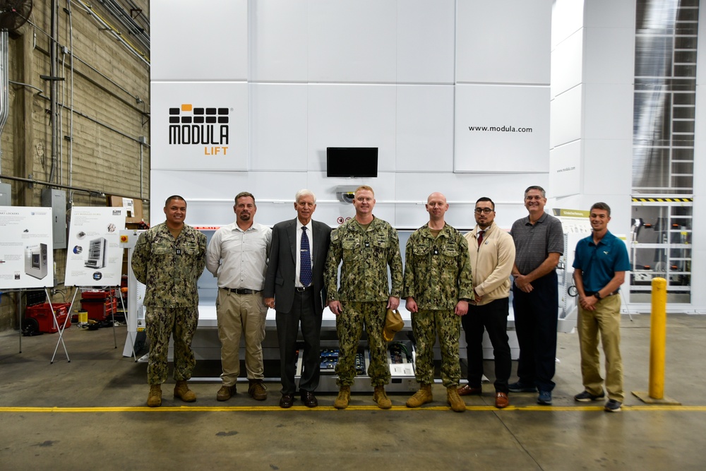 Capt. Cory Schemm and Executive Director Andrew Benson, NAVSUP Fleet Logistics Center San Diego,  gather with members of the 5G smart warehouse team to celebrate the commissioning of the vertical module lifts.