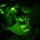 TACP Lightning Challenge 2022 A night vision image captured through a circular lens showing military personnel conducting nighttime operations. Two individuals wearing combat uniforms and headlamps are examining what appears to be a map or document on the ground. The image is rendered entirely in green monochrome tones characteristic of night vision optics.