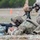 TACP Lightning Challenge 2022 Two soldiers in MultiCam/OCP camouflage uniforms are engaged in a marksmanship training exercise at an outdoor firing range. The prone shooter is firing an M4 carbine supported by sandbags, while a second soldier in a kneeling position observes downrange, likely acting as a spotter. A Leupold spotting scope on a tripod is visible between them, consistent with a precision marksmanship or qualification event.