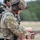 TACP Lightning Challenge 2022 A soldier or military/law enforcement operator in full tactical gear is inspecting or performing a press check on a tan/FDE semi-automatic pistol, consistent with a SIG Sauer P320 M17/M18. The individual is wearing MultiCam camouflage, a tactical helmet with communications headset, eye protection, and a plate carrier vest. The setting appears to be an outdoor shooting range or training exercise.