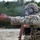 TACP Lightning Challenge 2022 A military or special operations personnel wearing TACP (Tactical Air Control Party) marked helmet and OCP/Multicam camouflage is firing a semi-automatic pistol at a shooting range. A spent brass casing is visible in the air above the weapon, indicating the firearm has just been discharged. The subject is equipped with full tactical gear including body armor, helmet-mounted devices, and a medical pouch.
