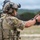 TACP Lightning Challenge 2022 A military or special operations personnel wearing full tactical gear is engaged in a pistol shooting exercise at an outdoor range. The individual is equipped with a JTAC-labeled helmet, multicam camouflage uniform, plate carrier vest, and communications headset. Additional personnel are visible in the background, suggesting a group training event.
