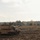 Bull Battery M109A7 Paladin Howitzers take to the field A self-propelled artillery vehicle, consistent with an M109 Paladin howitzer, is positioned on a sandy, churned terrain during what appears to be a military exercise or training operation. The vehicle is painted in a desert tan/sand camouflage scheme and has its barrel extended horizontally. The background features a treeline with autumn foliage, suggesting a temperate European or North American training environment.