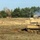 Bull Battery M109A7 Paladin Howitzers take to the field A military training or combat exercise scene showing multiple self-propelled artillery systems deployed across an open sandy terrain. At least two M109 Paladin self-propelled howitzers are visible, with one in the foreground and others in the background, with visible gun smoke indicating recent or active firing. A military utility vehicle (likely an LMTV or similar) is also present on the left side of the image.