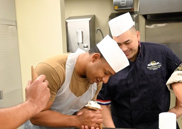 CSSN Albert Velasquez from USS John Canley (ESB-6), demonstrates his cake border technique to CS1 (SW/AW) Suriya Chuon.