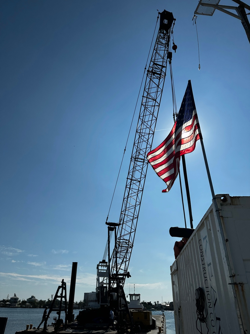 A Flag Blows Before A Crane Which is Transporting Destroyed Vessels