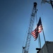 A Flag Blows Before A Crane Which is Transporting Destroyed Vessels