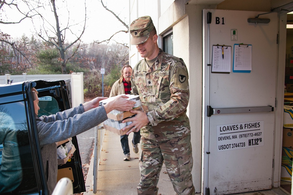 Zach Desautels hands a stack of canned good to LTC Trent Colestock, Garrison Commander, as they unload one van at the food drive drop off.