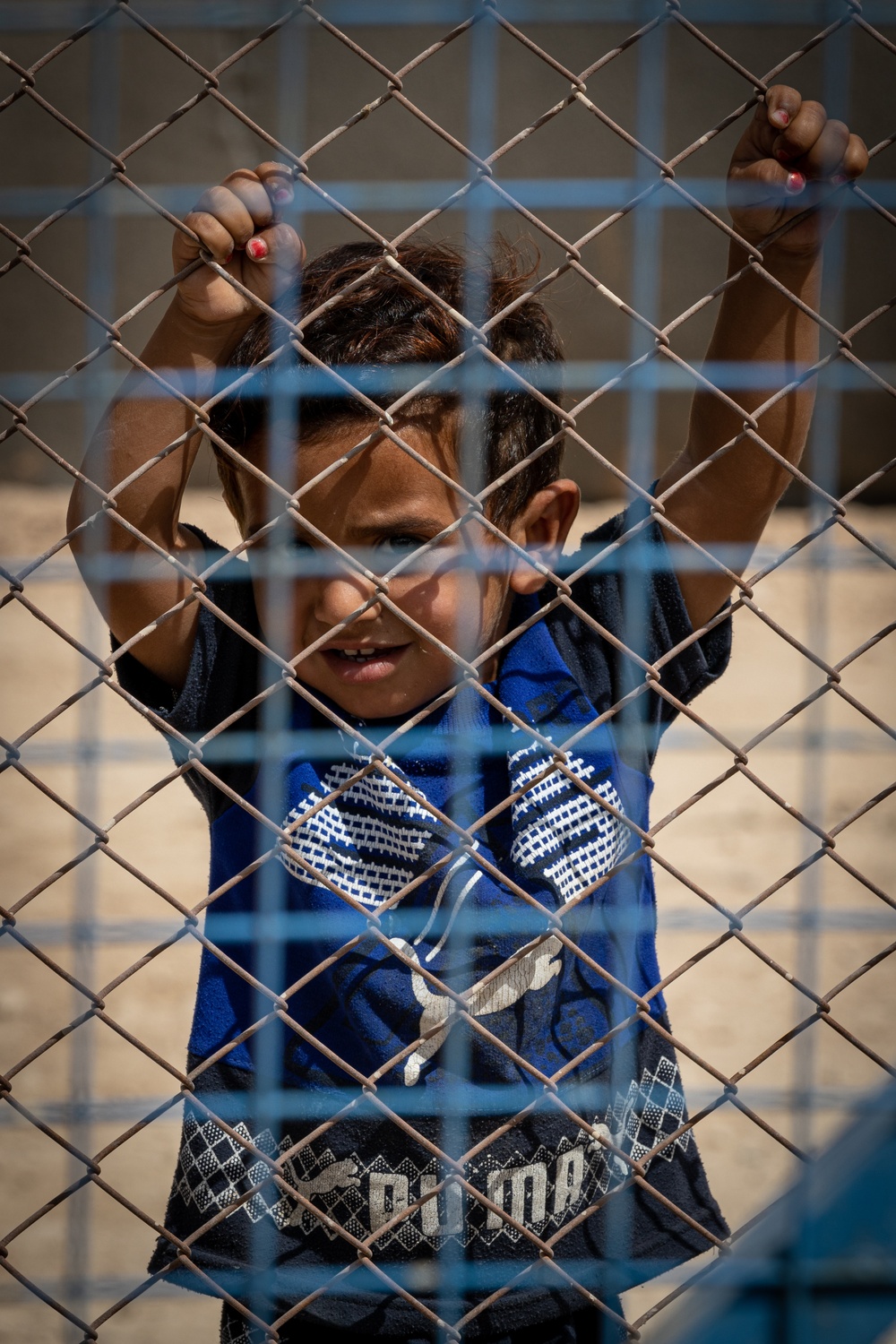 A boy peers through the fence line at al Hol camp during a US Civil Affairs team visit