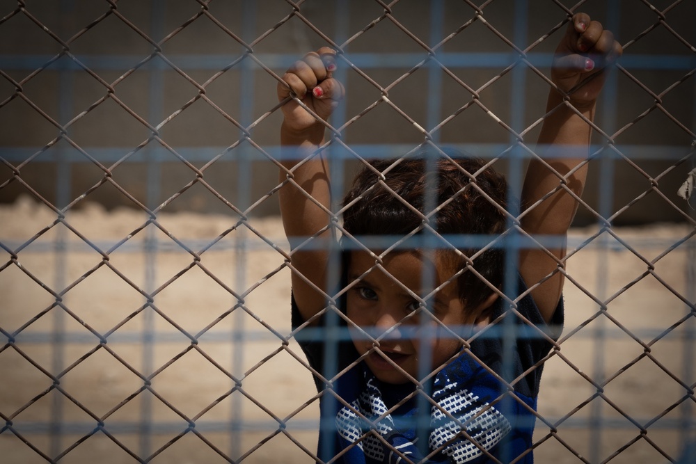 A young child peers through the fence at al Hol camp during a US Civil Affairs team visit