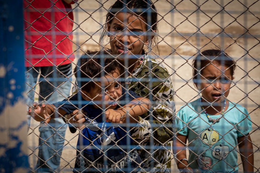 Children look to a US Civil Affairs team through the fence at al Hol camp